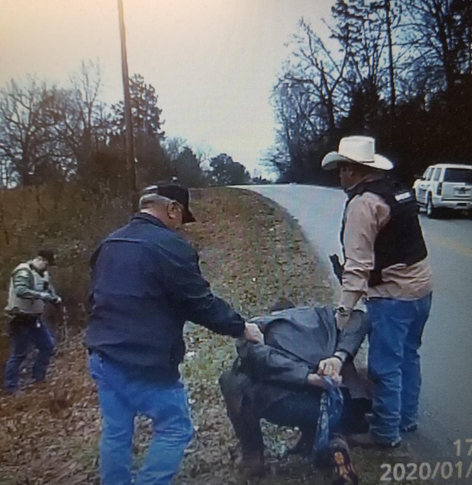 two men holding arrested man in cuffs