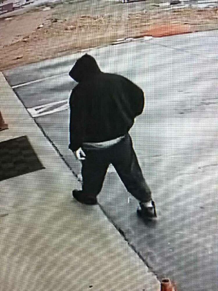 Camera footage of a man dressed in a black hoodie, black sweatpants, and black sneakers walking towards a building.